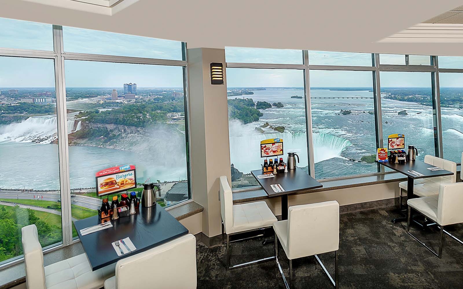 A restaurant overlooking Niagara Falls, with multple tables availabe along the windows.