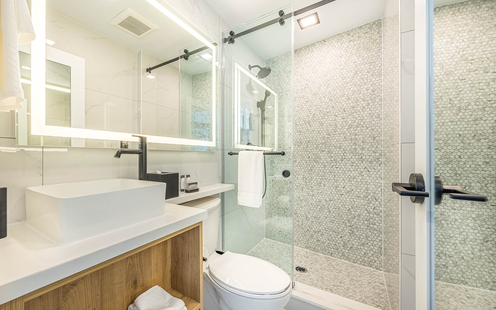 A sleek modern bathroom featuring a glass shower door, tiled shower wall, white sink and black faucets