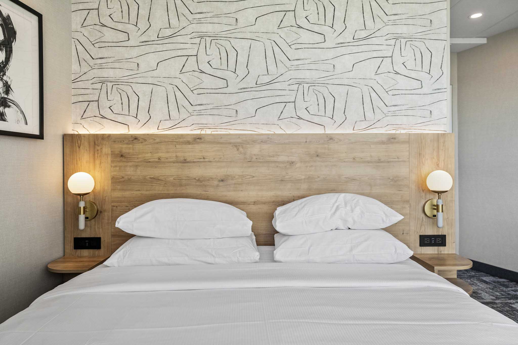 A hotel room with a king bed with white linen and a spacious desk for work or study purposes.