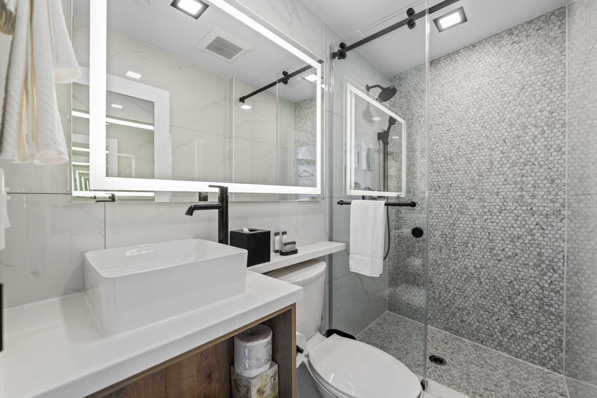 A sleek modern bathroom featuring a glass shower door, tiled shower wall, white sink and black faucets