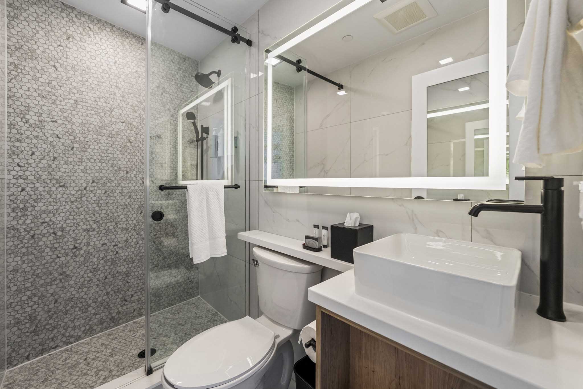 A sleek modern bathroom featuring a glass shower door, tiled shower wall, white sink and black faucets